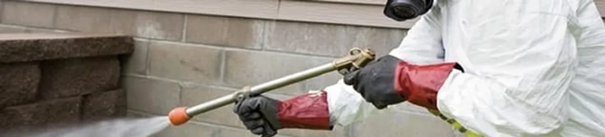 Pest control technician applying exterior insect treatment along a home foundation in Long Beach, CA