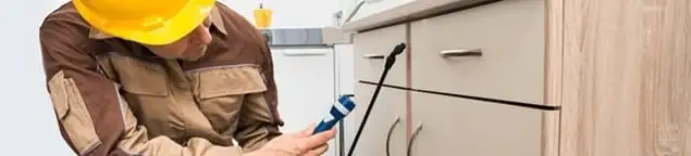 Roach exterminator applying treatment under kitchen cabinets in Long Beach, CA