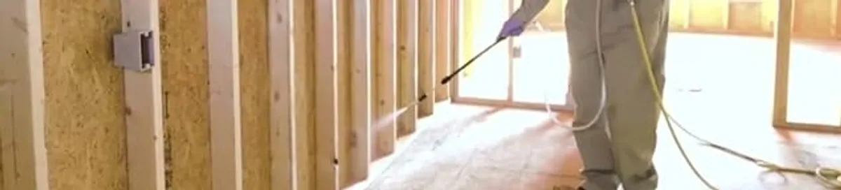 Termite treatment technician applying spray along framing and unfinished walls in Long Beach, CA