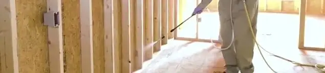 Termite treatment technician applying spray along framing and unfinished walls in Long Beach, CA